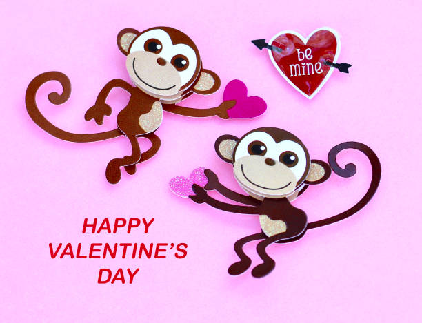 two monkeys holding hearts smiling on a pink background with happy valentines day message