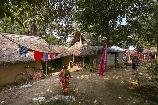 West Bengal, India, November 2,2019: Tribal woman bringing water to her mud house with view of inner courtyard at an Indian village at Bolpur, West Bengal