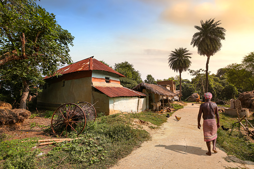 West Bengal, India, November 2,2019: Rural man walking along an unpaved village road with view of mud houses at sunset. Photograph shot at Bolpur, West Bengal India