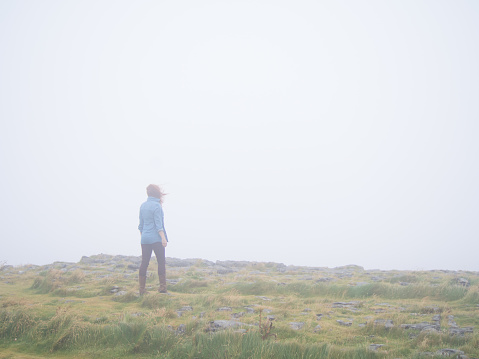 A lone woman walks across a lush field in a heavy haze.