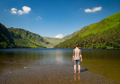Handsome man ventures into a stunning lake surrounded by a beautiful green mountain range.
