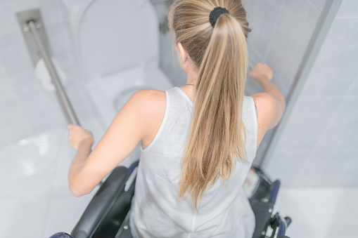 Young woman sitting in a wheelchair grabs the handrails for the disabled. Accessibility concept.