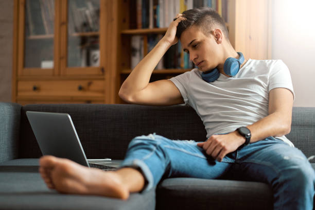 istock Young handsome man with laptop on gray sofa at home 1202014498
