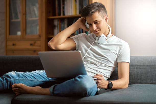 istock Young handsome man with laptop on gray sofa at home 1202014514