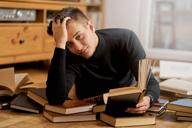 istock Young handsome student learns on the floor with books for exam 1202015020