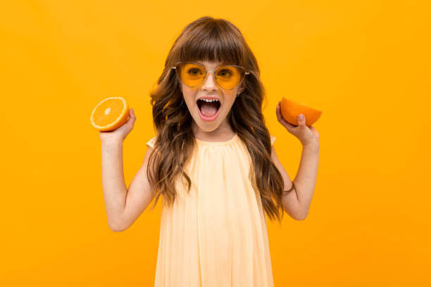 istock joyful girl with oranges on a yellow background 1202016896