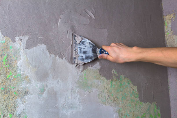 istock Plaster the wall with a putty knife.Internal construction and finishing works.The Builder puts plaster on the wall.Hand holding a spatula with construction mix and smoothes out bumps.Repair the wall 1202017051