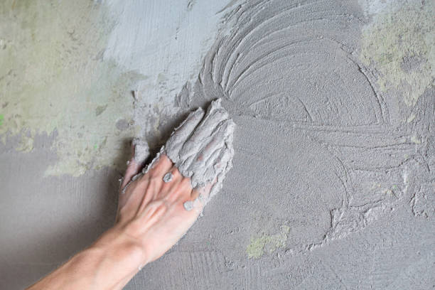 istock The plasterer Builder puts the plaster on the wall with his hand. Internal construction and finishing works.The hand holds the construction mix and smoothes the roughness on the wall 1202017093