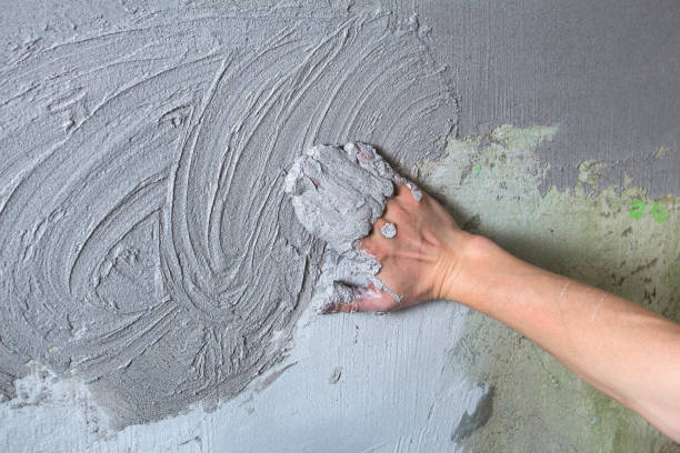 istock The plasterer Builder puts the plaster on the wall with his hand. Internal construction and finishing works.The hand holds the construction mix and smoothes the roughness on the wall 1202017100