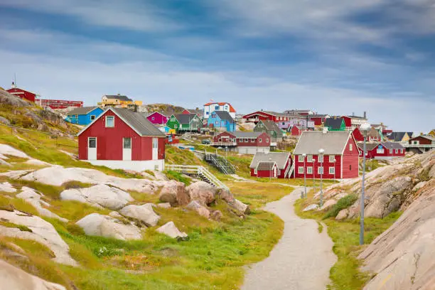 Ilulisaat colorful houses city - town view along sandy footpath between rocky landscape under blue summer skyscape. Ilulissat, Western Greenland, Greenland, Europe.