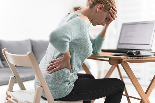 Mujer trabajando en un ordenador portátil y tener dolor de cabeza y espalda, cadera, dolor de columna vertebral. photo