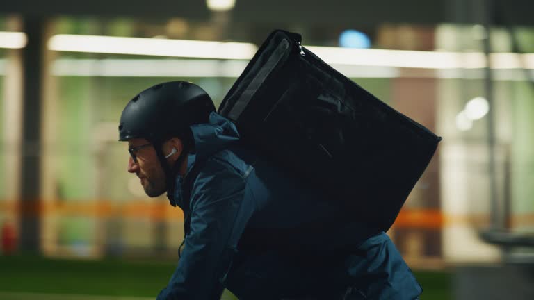 Slow motion of an young delivery courier with bicycle is touching a futuristic screen with augmented reality hologram maps to view the addresses of customers in the evening in a city center