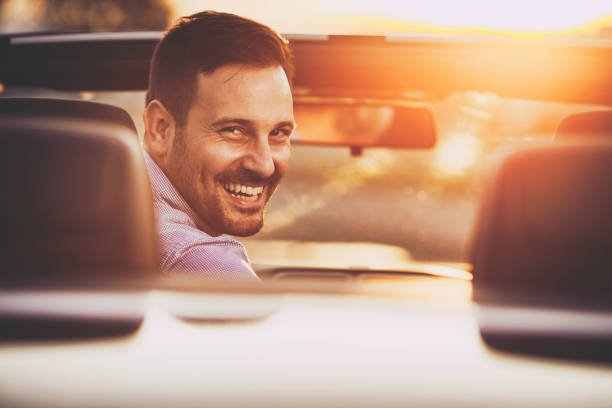 jeune homme heureux dans la voiture convertible au coucher du soleil. - car driving men reversing photos et images de collection