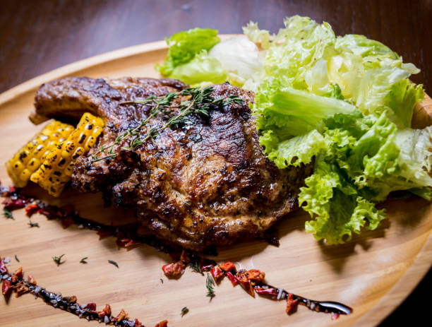 istock Pork grilled ribs with corn and salad on a wooden board. 1202035034