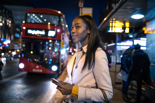 Woman at bus stop in the night in London, waiting for her connection to home.