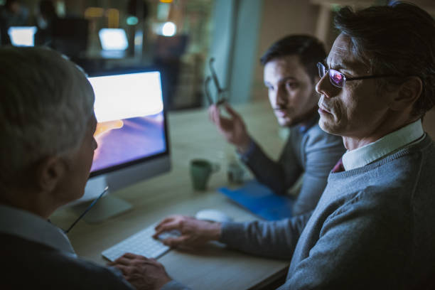 istock Business colleagues talking while working on desktop PC at dark office. 1202039500