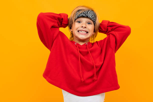 istock blond boy with a bandana on his head in a red jacket grimaces on an orange wall 1202041048