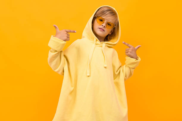 istock blond boy with a panama in a light hoodie with glasses posing on a orange studio background 1202041059