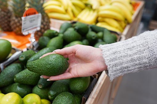 Cropped image of a customer choosing avocados in the supermarket. close up of woman hand holding avocado in market.