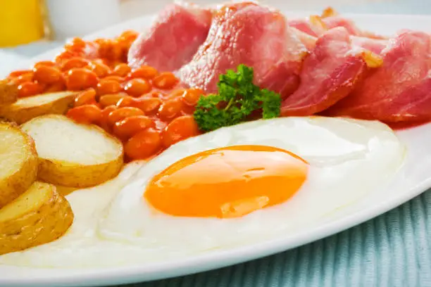 English breakfast of bacon, fried egg, saute potatoes and baked beans.