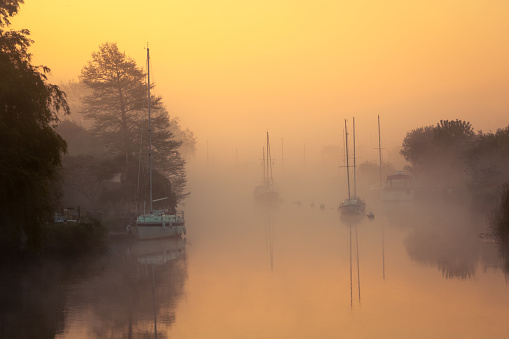 Boats appear from the early morning mist on the Wareham River, Dorset, England,