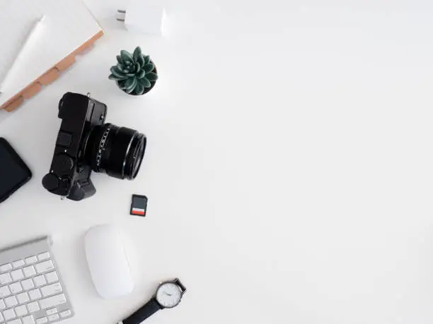 Photo of top view of photographer work station, work space concept with digital camera, memory card, keyboard and smartphone on white table background