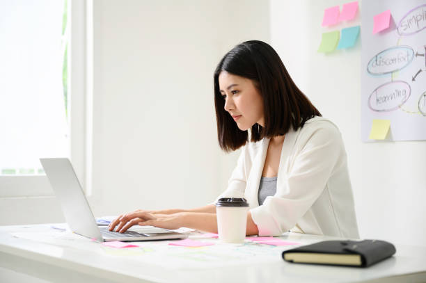 istock Young asian business woman working on computer laptop in office room with paperwork document on desk 1202057053
