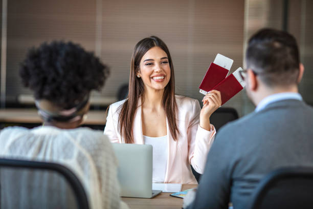 The travel agent keeps tickets for the plane in the travel agency. The travel agent keeps tickets for the plane in the travel agency.  She offers them to clients. Couple at the travel agency office prepairing for a summer vacation. Concept for travel agent. travel agency stock pictures, royalty-free photos & images