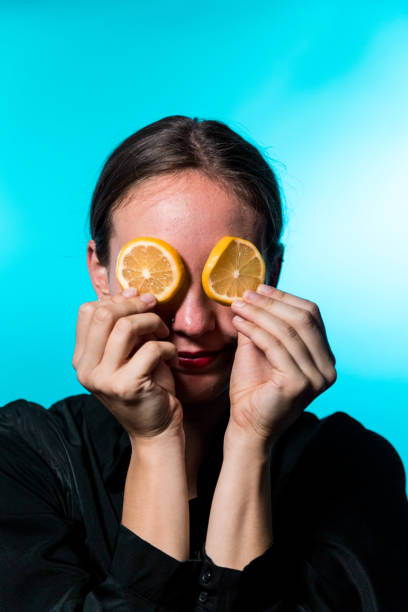 istock Young Woman with Lemon Slices Over Eyes on Blue Background 1202064841
