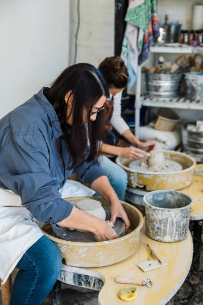 istock two ceramic artists working side by side at pottery wheels in an art studio throwing clay pots on pottery wheels trimming their pots 1202066759