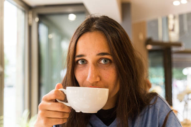 istock Young Woman with Coffee Mug on Lips Looking at Camera 1202066827