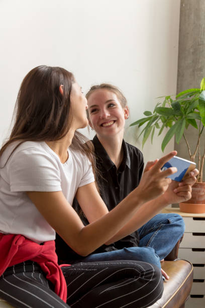 istock Two Young Women Making Eye Contact and Smiling on Couch 1202073937