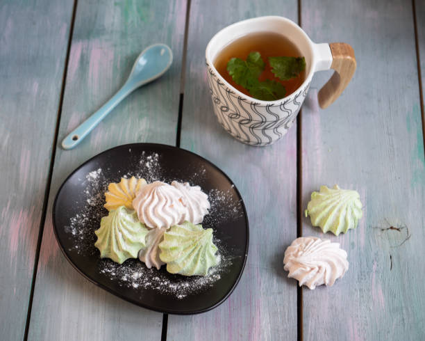istock Marshmallow of different colors on a black plate and a decorative mug with green tea on a wooden tray 1202073967
