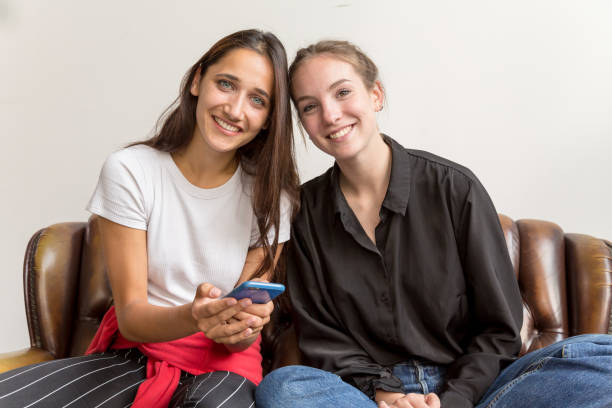 istock Two Young Women Seated Side by Side on Sofa Looking at Camera and Smiling 1202075828