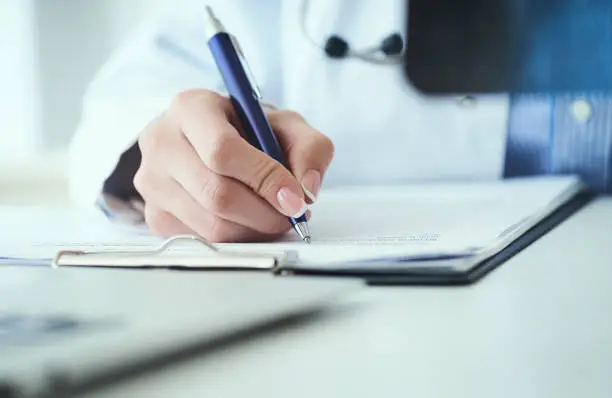 Photo of Close up of female doctor holding x-ray or roentgen image and making notes in medical form.