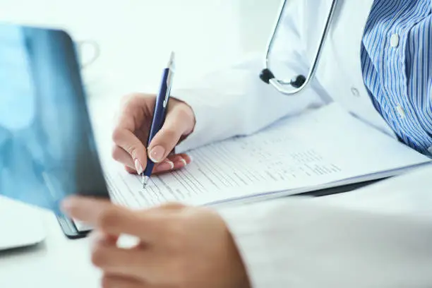 Photo of Close up of female doctor holding x-ray or roentgen image and making notes in medical form.