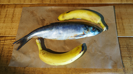 Close-up delicious salted herring and two yellow bananas on the old wooden background. Rustic style.