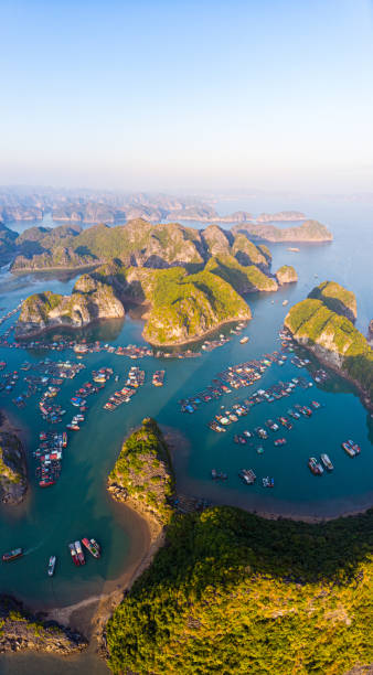 aerial sunset view of lan ha bay and cat ba island, vietnam, unique limestone rock islands and karst formation peaks in the sea, floating fishermen villages and fish farms from above. clear blue sky. - halong bay vietnam bay cruise imagens e fotografias de stock