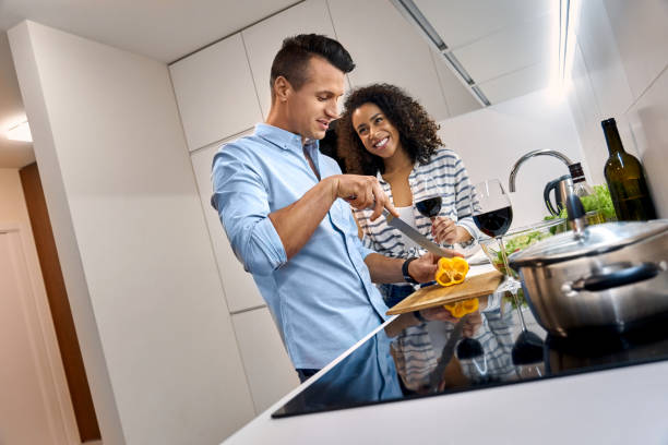 Romantic Date. Young multiethnic couple standing at kitchen cooking dinner wife drinking wine while husband cutting vegetables smiling concentrated