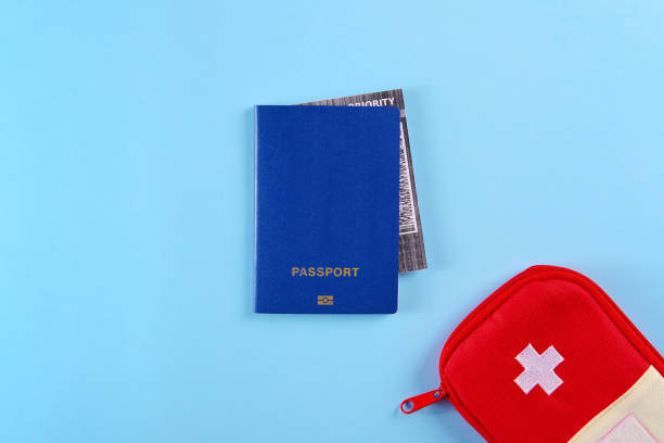 istock Blue external passport with airplane ticket inside and red travel first aid kit pouch on the bright blue background 1202090421