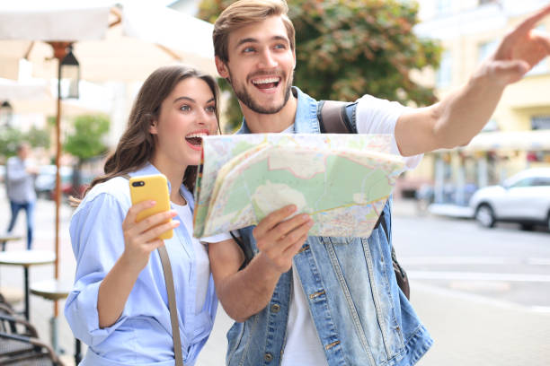 istock Beautiful young couple holding a map and smiling while standing outdoors. 1202092047
