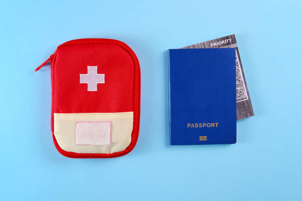 istock Blue external passport with airplane ticket inside and red travel first aid kit pouch on the bright blue background 1202093221