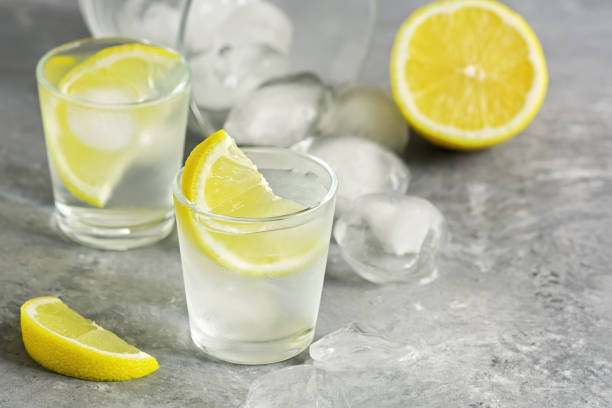 bicchiere a colpo di vodka con ghiaccio e succose fette di limone su uno sfondo di cemento grigio. alcol tradizionale russo. messa a fuoco selettiva, spazio di copia. - russian shot foto e immagini stock