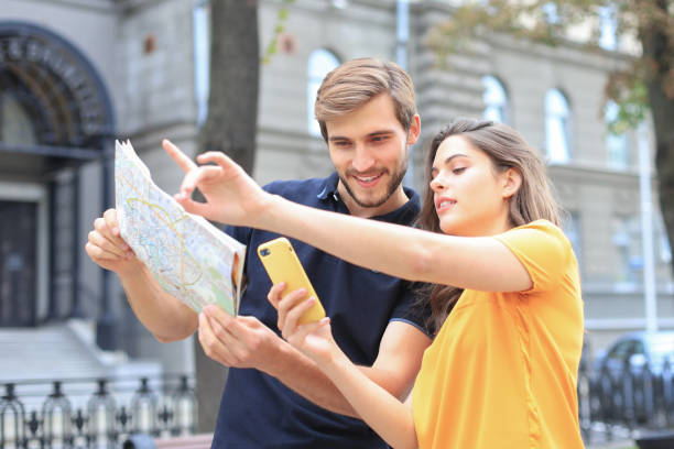 istock Beautiful young couple holding a map and smiling while standing outdoors. 1202093645