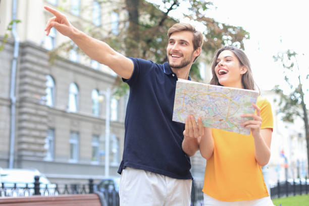 istock Beautiful young couple holding a map and smiling while standing outdoors. 1202093665