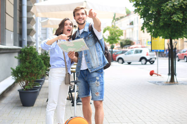 istock Beautiful young couple holding a map and smiling while standing outdoors. 1202094689