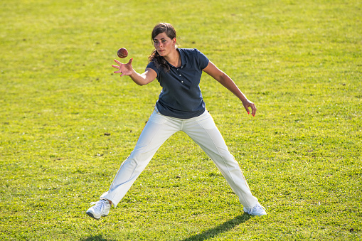 Photo of a female cricket player on the grass moments before catching the ball.
