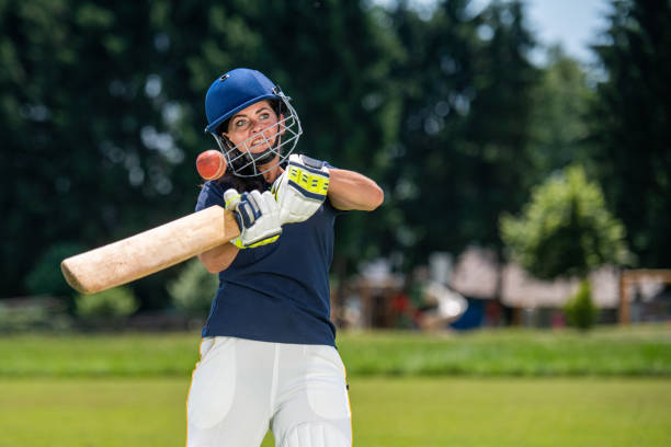 Female cricket player hitting the ball with a bat Front view photo of a female cricket player in mid-stroke while batting the ball. batsman photos stock pictures, royalty-free photos & images