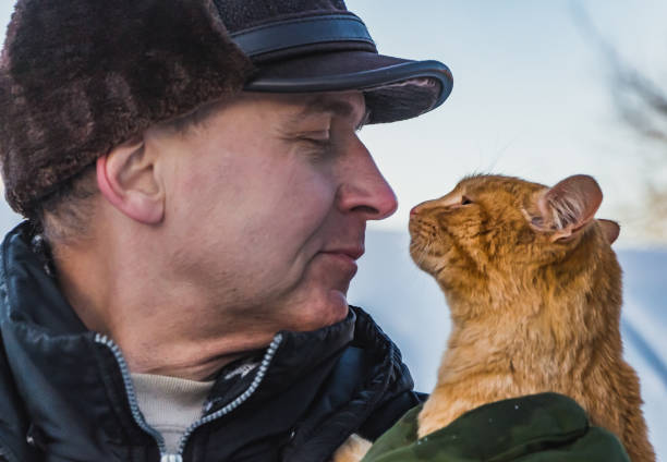 A middle-aged man in a brown hat and a red cat look at each other in a winter garden