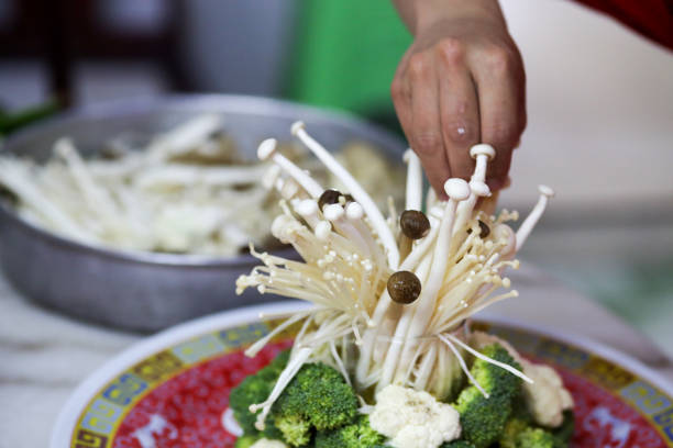 A closer look on human hand using enoki mushroom for garnishing as part of food preparation in Malaysia.